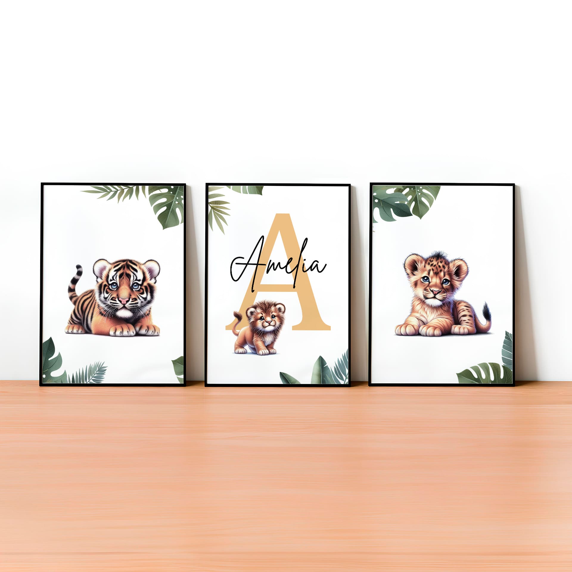 Set of three A4 prints featuring baby big cats - lion cub, tiger cub, and cheetah cub. The animals are depicted in a cartoony, bright style, resembling coloured pencil drawings. Jungle-style leaves adorn the edges of the prints. The middle print features a smaller animal compared to the others, with a large initial letter in the background. A personalised name in black overlays the initial letter.