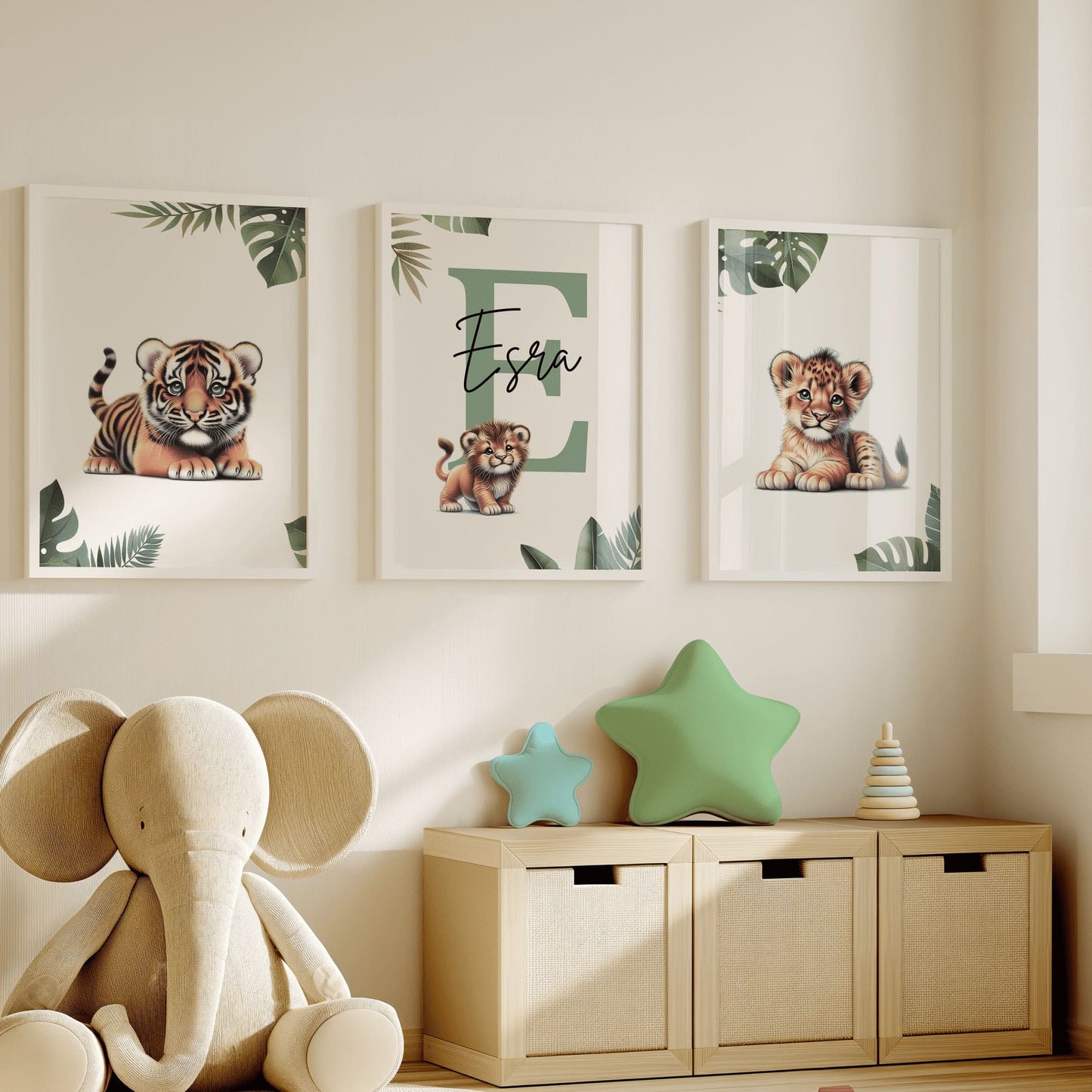 Set of three A4 prints featuring baby big cats - lion cub, tiger cub, and cheetah cub. The animals are depicted in a cartoony, bright style, resembling coloured pencil drawings. Jungle-style leaves adorn the edges of the prints. The middle print features a smaller animal compared to the others, with a large initial letter in the background. A personalised name in black overlays the initial letter.