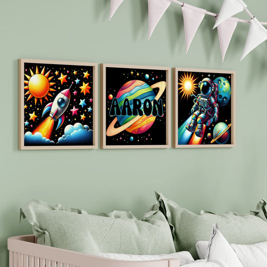 Set of Three Square Nursery Prints. Black background with bright colourful images with a space theme - astronaut, rocket, planet. One print is personalised with a name