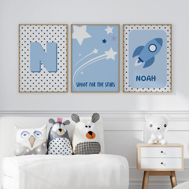 3 Nursery Prints in Blue. One features spotty background with childs initial, one with simple stars on blue background, one with a rocket and childs name