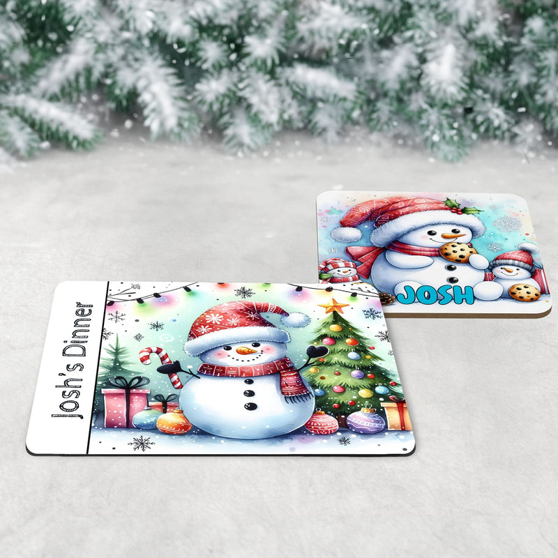 3 piece childrens Christmas dinner table set - a placemat, coaster and mug featuring bright and fun snowman designs, one drinking hot chocolate, one eating cookies and one with a tree and decorations. All personalised with childs name