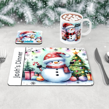 3 piece childrens Christmas dinner table set - a placemat, coaster and mug featuring bright and fun snowman designs, one drinking hot chocolate, one eating cookies and one with a tree and decorations. All personalised with childs name