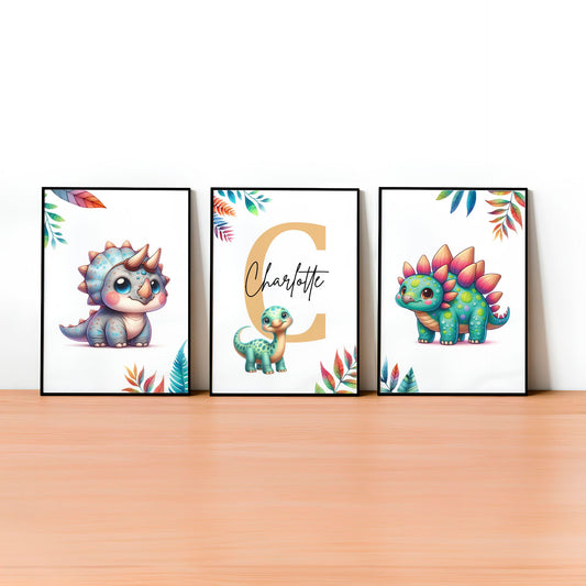 Set of three A4 prints featuring cute baby dinosaurs. The dinosaurs are depicted in a cute, cartoony, bright style resembling coloured pencil drawings. Rainbow coloured leaves decorate the edges of the prints. The middle print features a smaller dinosaur than the others, with a large initial letter in the background. A personalised name in black overlays the initial letter.