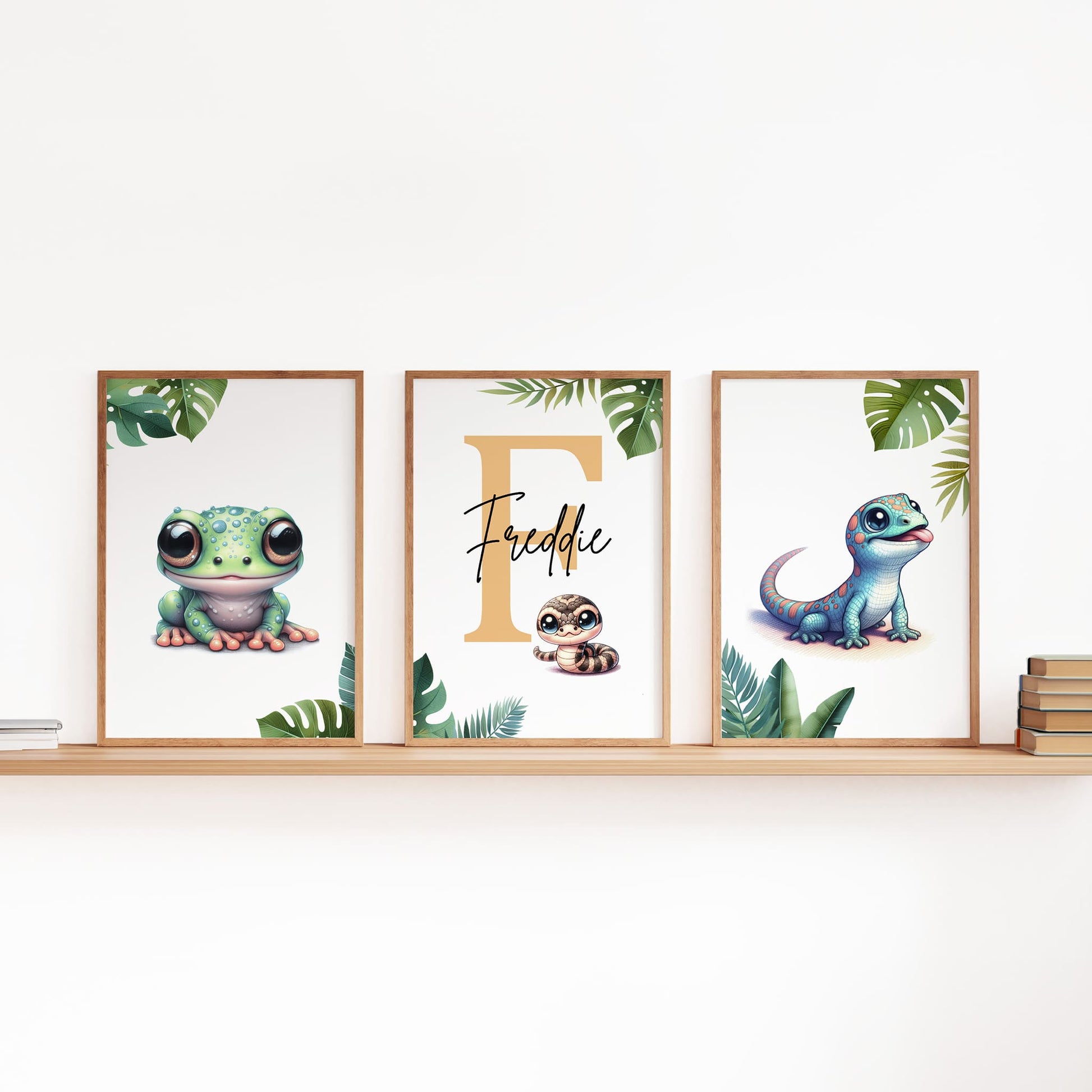 Set of three A4 prints featuring reptiles/amphibians - tree frog, lizard, and snake. The animals are depicted in a cartoony, bright style resembling coloured pencil drawings. Jungle-style leaves decorate the edges of the prints. The middle print features a smaller animal than the others, with a large initial letter in the background. A personalised name in black overlays the initial letter.