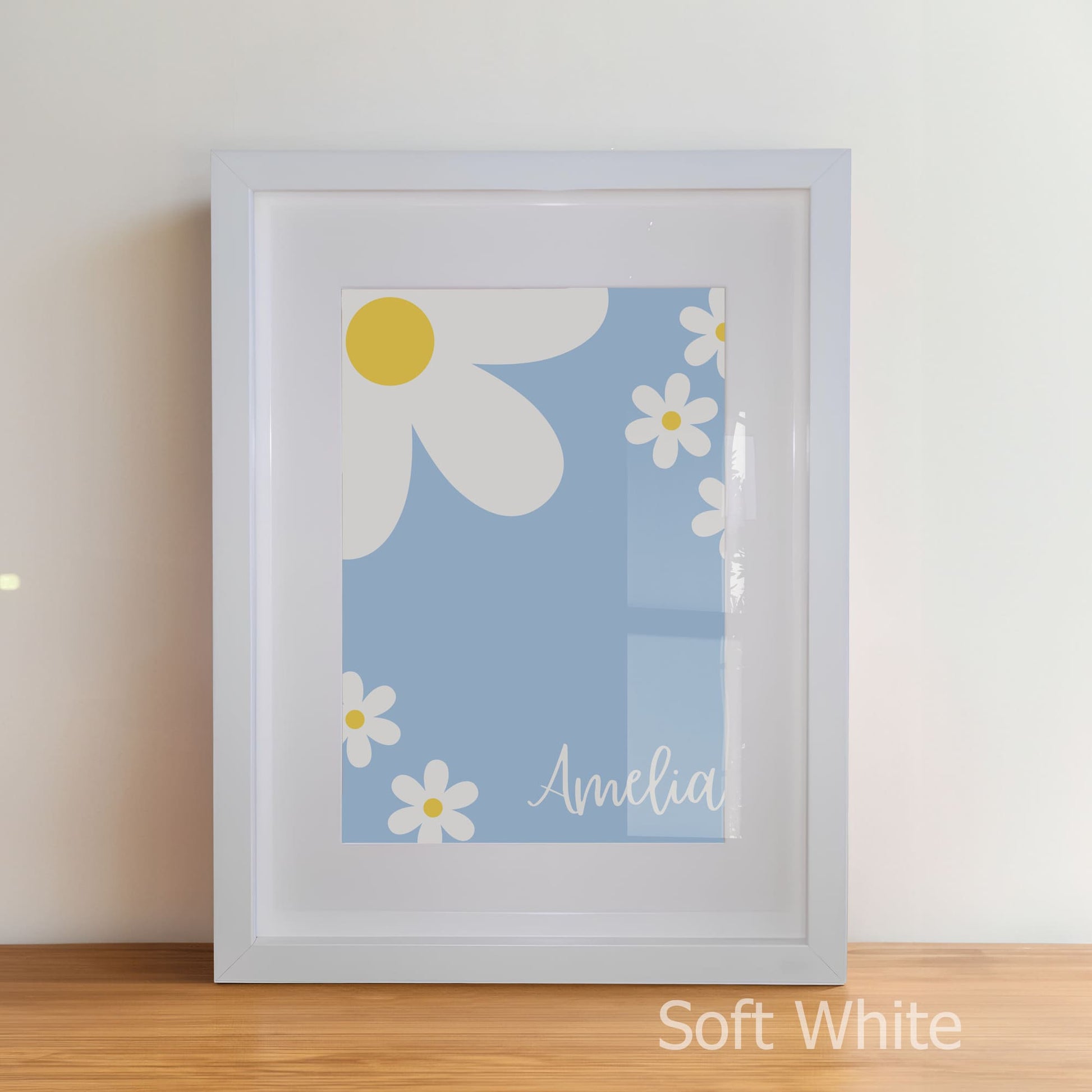Framed artwork with daisy design and name 'Amelia' on a light blue background, in soft white frame.