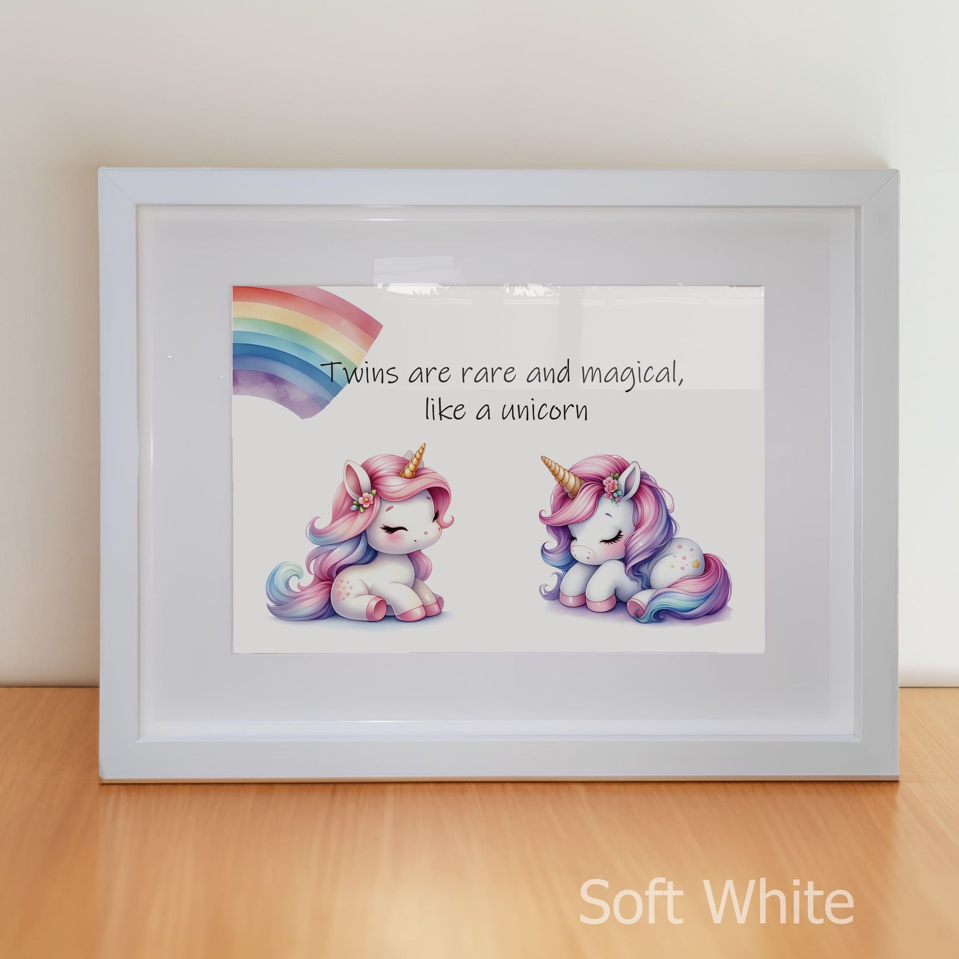 Framed artwork with two cartoon unicorns and a rainbow, text 'Twins are rare and magical, like a unicorn', on a light wooden surface.