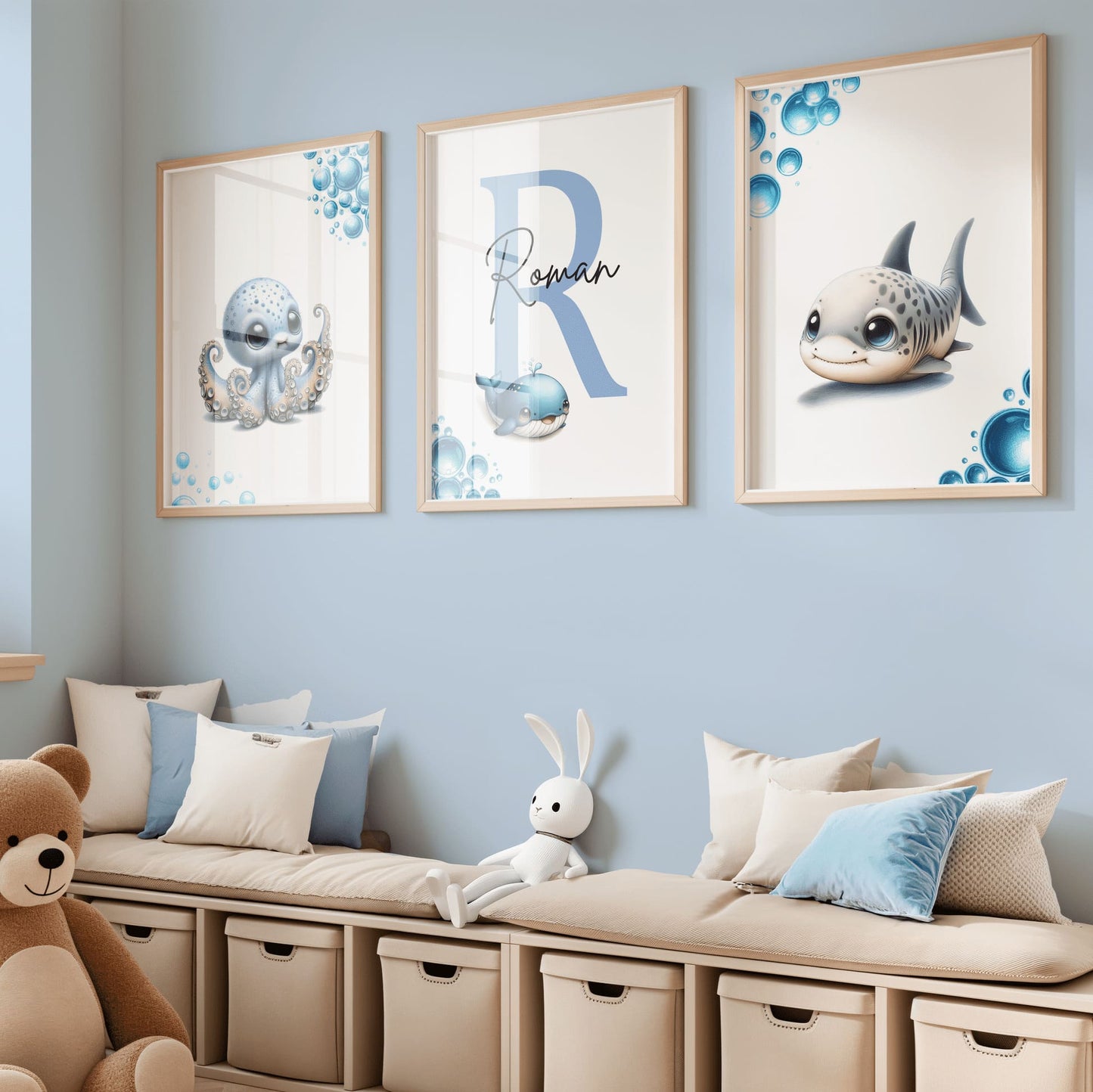 Set of three A4 prints featuring baby ocean animals - whale, shark, and octopus. The animals are depicted in a cute, cartoony, bright style resembling coloured pencil drawings. Blue bubbles decorate the edges of the prints. The middle print features a smaller animal than the others, with a large initial letter in the background. A personalised name in black overlays the initial letter.