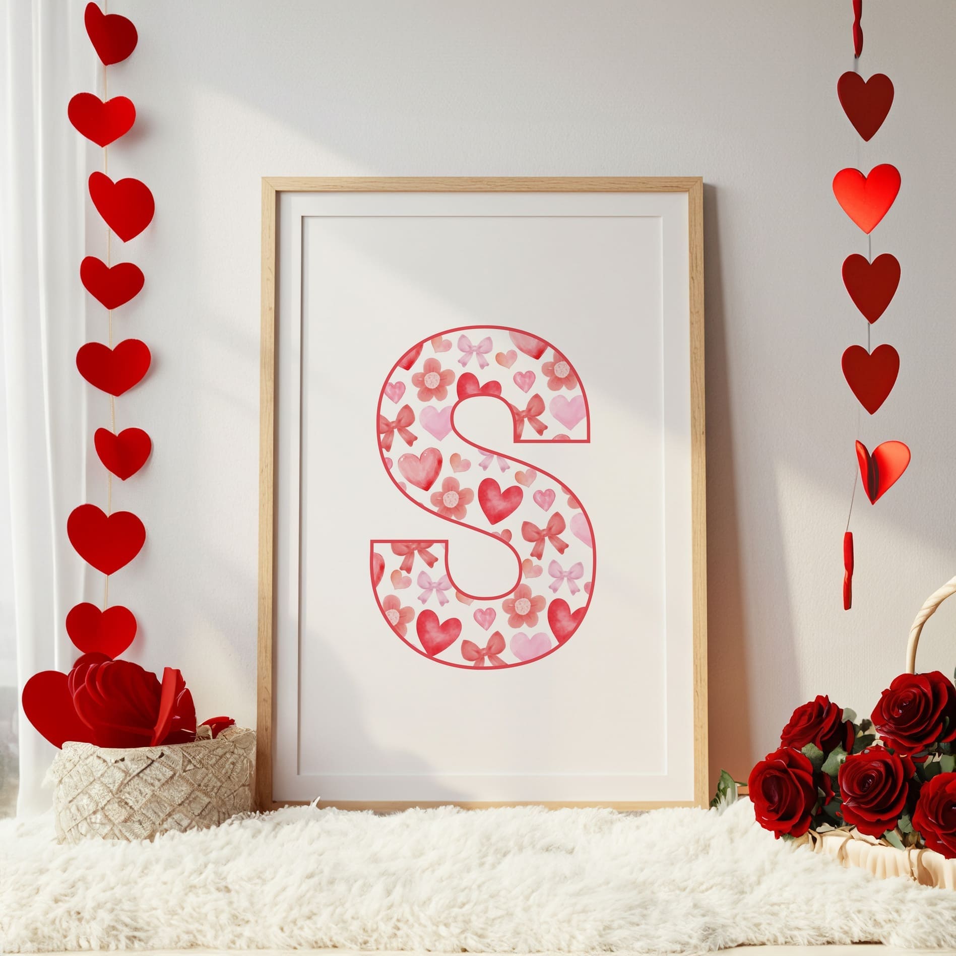 Framed artwork with a decorative letter 'S' surrounded by heart shapes and flowers on a white surface.