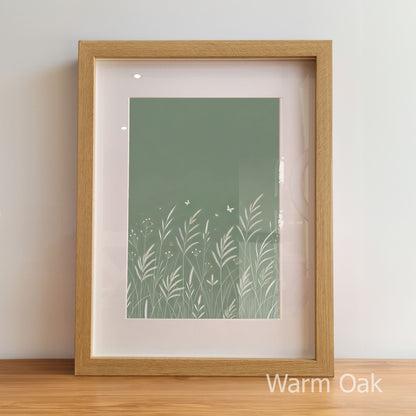 Framed artwork with a green nature-themed print inside, on a wooden floor.