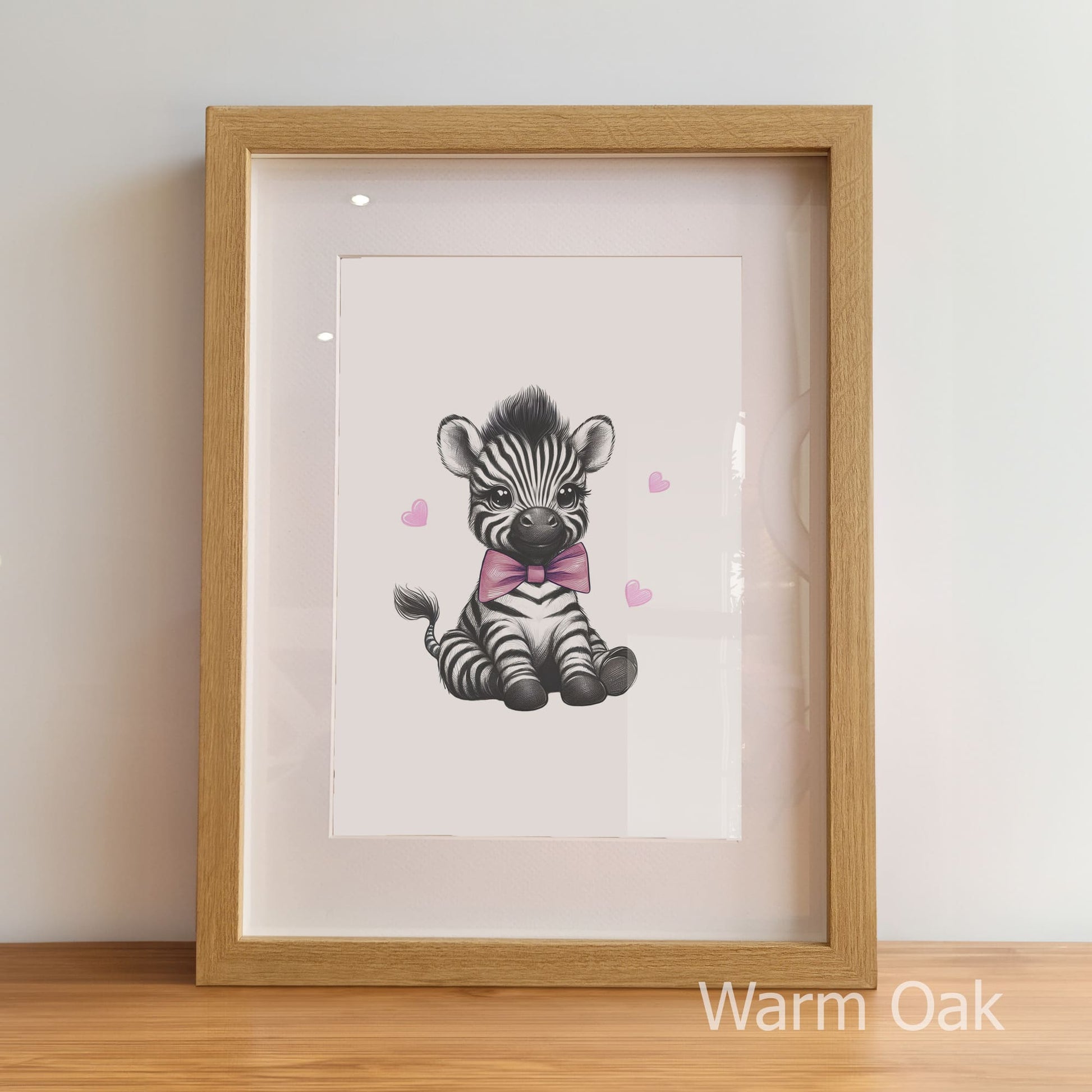Framed artwork of a zebra with a pink bow tie on a white background, displayed on a wooden floor.