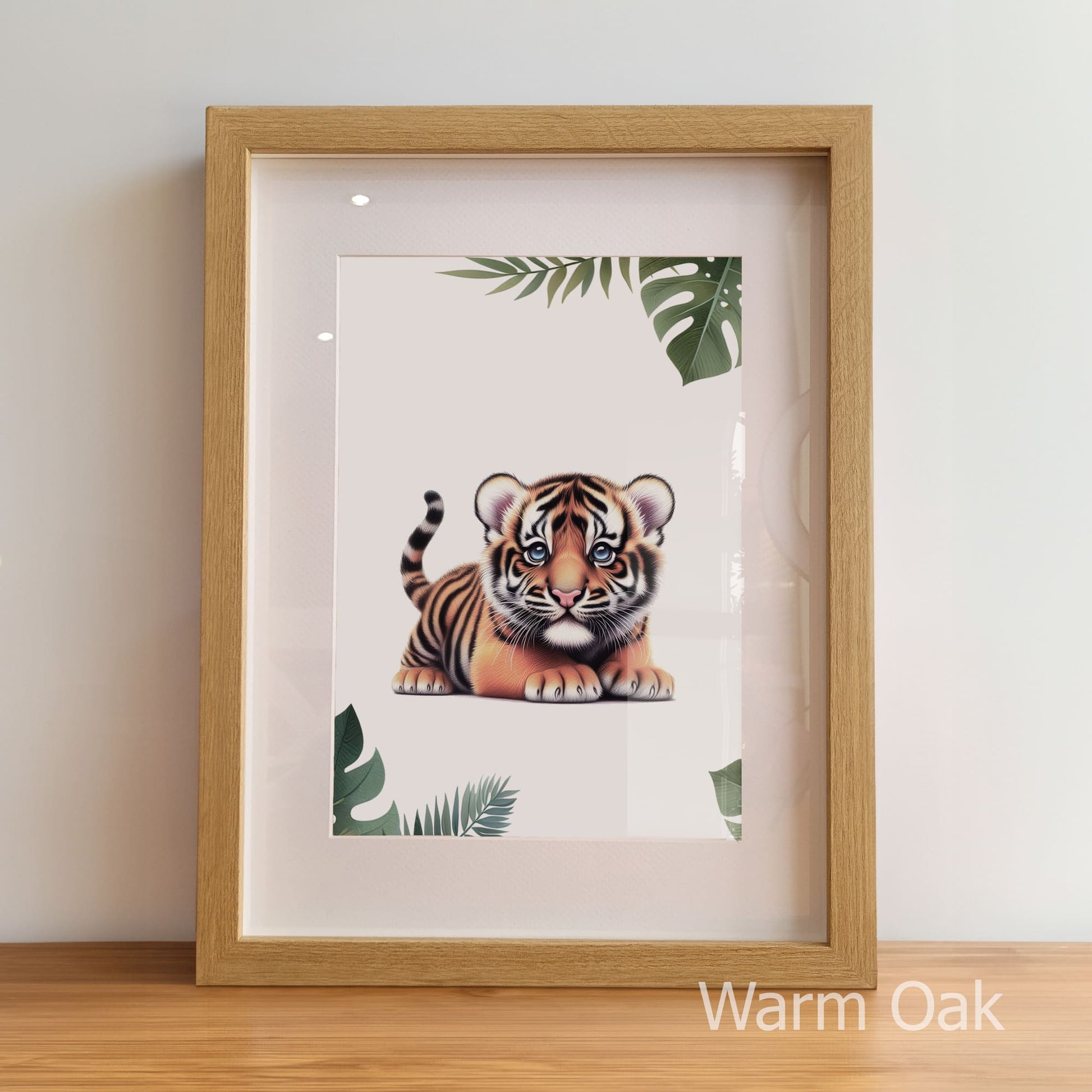 Framed artwork of a tiger cub with green leaves on a white background, displayed on a wooden surface.