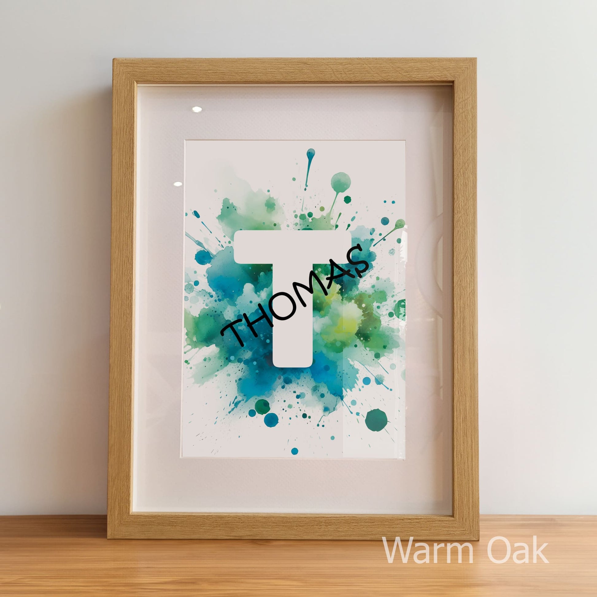 Framed artwork with 'THOMAS' on a watercolor background, displayed on a wooden surface.