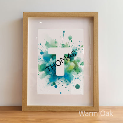 Framed artwork with 'THOMAS' on a watercolor background, displayed on a wooden surface.