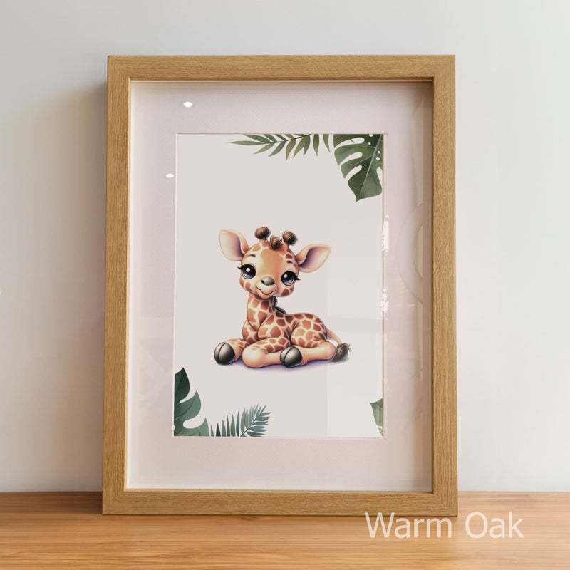 Framed artwork of a baby giraffe with leaves on a white background, displayed on a wooden surface.