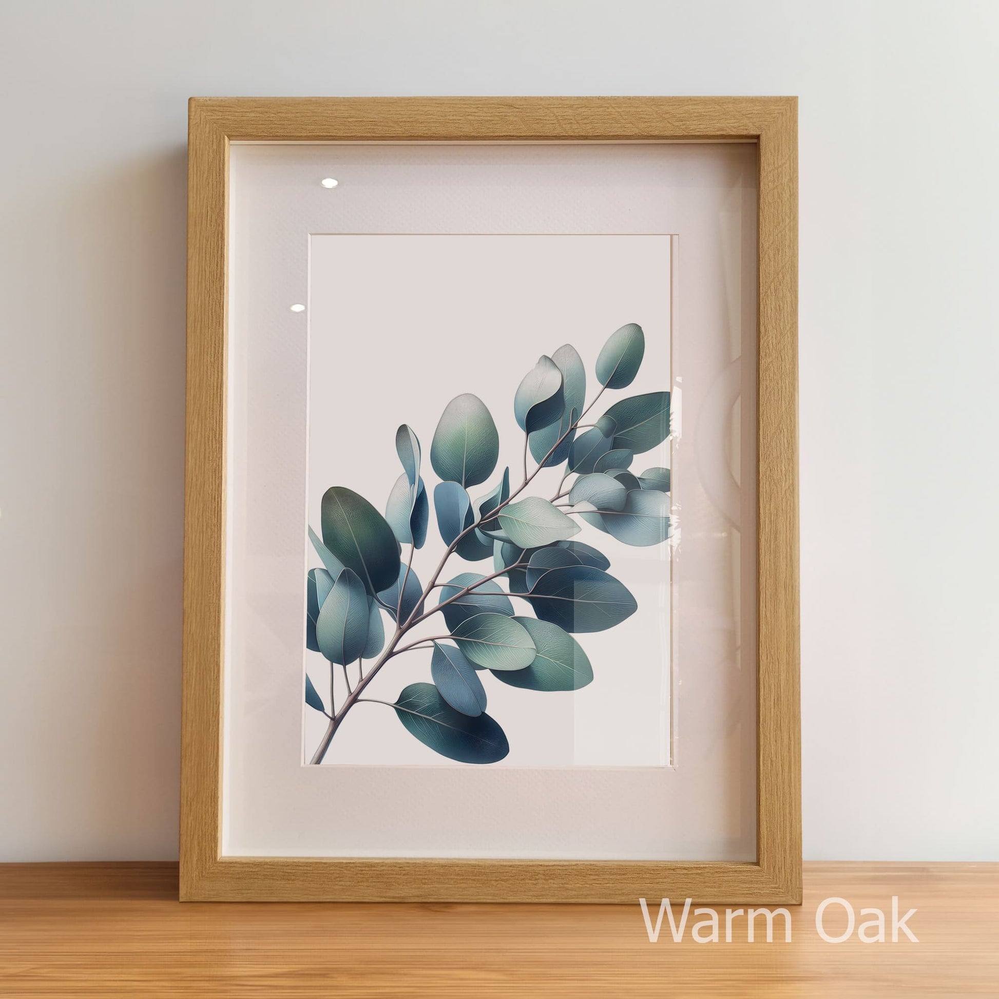 Framed artwork of a leafy branch with a warm oak frame on a light background
