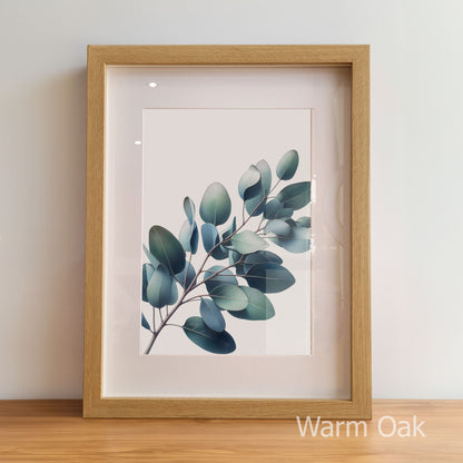 Framed artwork of a leafy branch with a warm oak frame on a light background