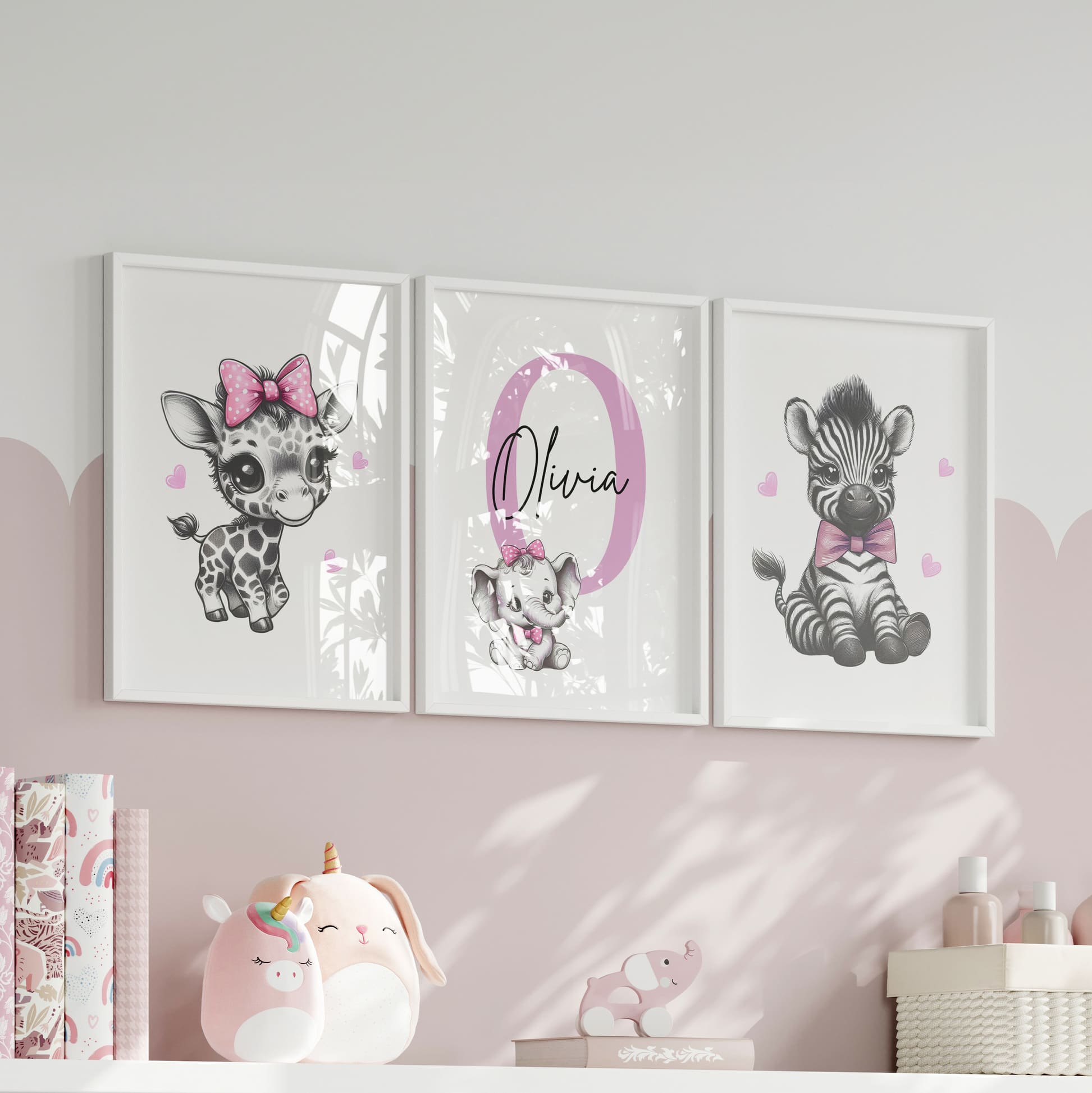 Set of three A4 prints in the style of pencil drawings. Each print features a cartoon baby giraffe, baby elephant, and baby zebra in black and white. They all wear a pink bow, with a few small pink hearts in the background. The middle image contains the elephant, which is smaller than the other two images. In the background, there is a large initial with a personalised name in black.