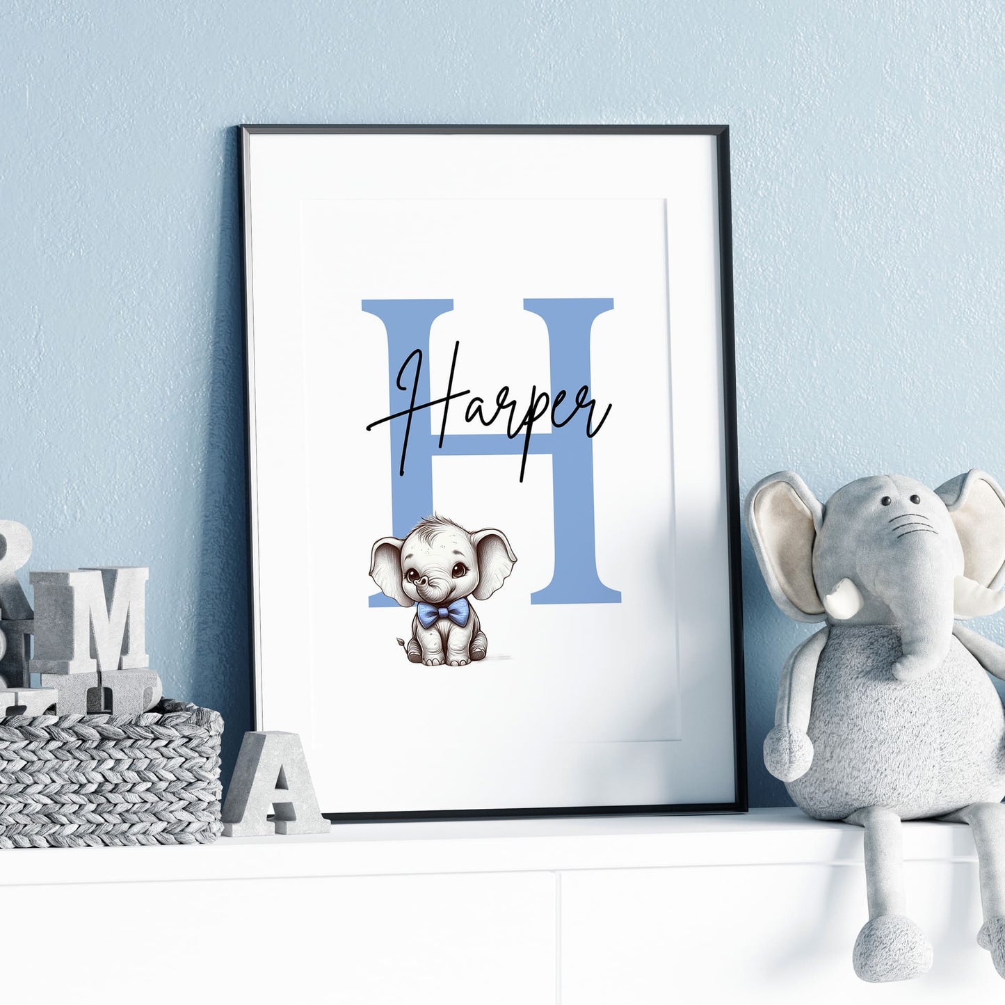 Set of three A4 prints in the style of pencil drawings. Each print features a cartoon baby giraffe, baby elephant, and baby zebra in black and white. They all wear a blue bow, with a few small blue hearts in the background. The middle image contains the elephant, which is smaller than the other two images. In the background, there is a large initial with a personalised name in black.