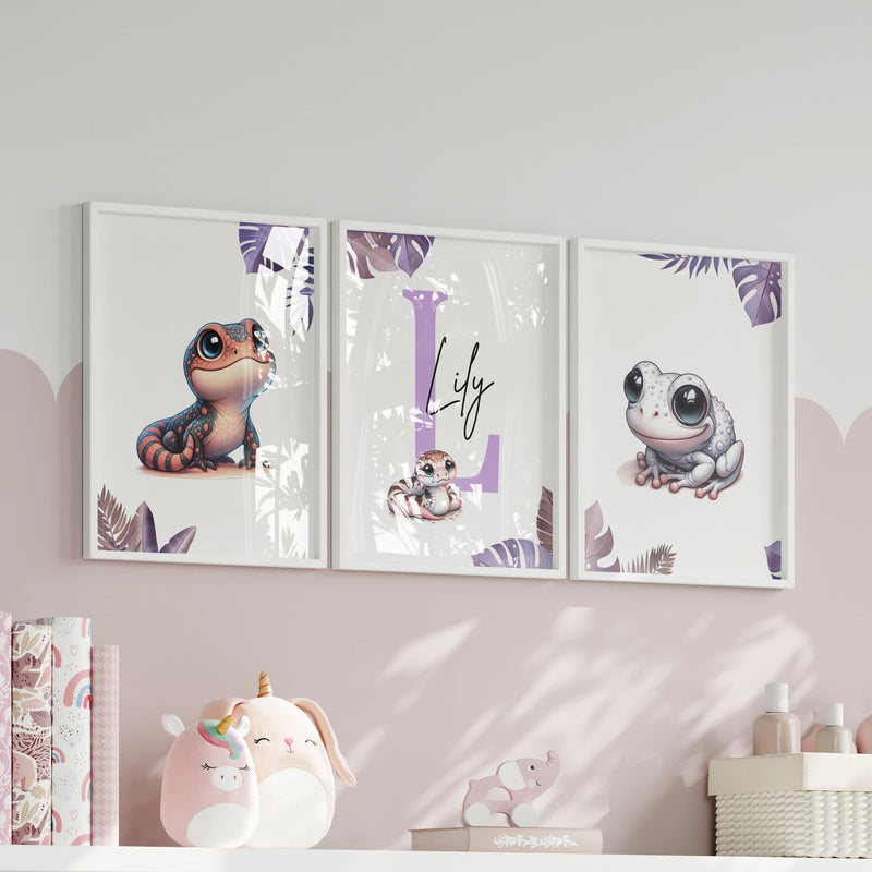Set of three A4 prints featuring pink/purple reptiles/amphibians - frog, lizard, and snake. The animals are depicted in a cartoony, style resembling coloured pencil drawings in warm shades of pink, purple and orange. Jungle-style leaves in shades of purple decorate the edges of the prints. The middle print features a smaller animal than the others, with a large initial letter in the background. A personalised name in black overlays the initial letter.